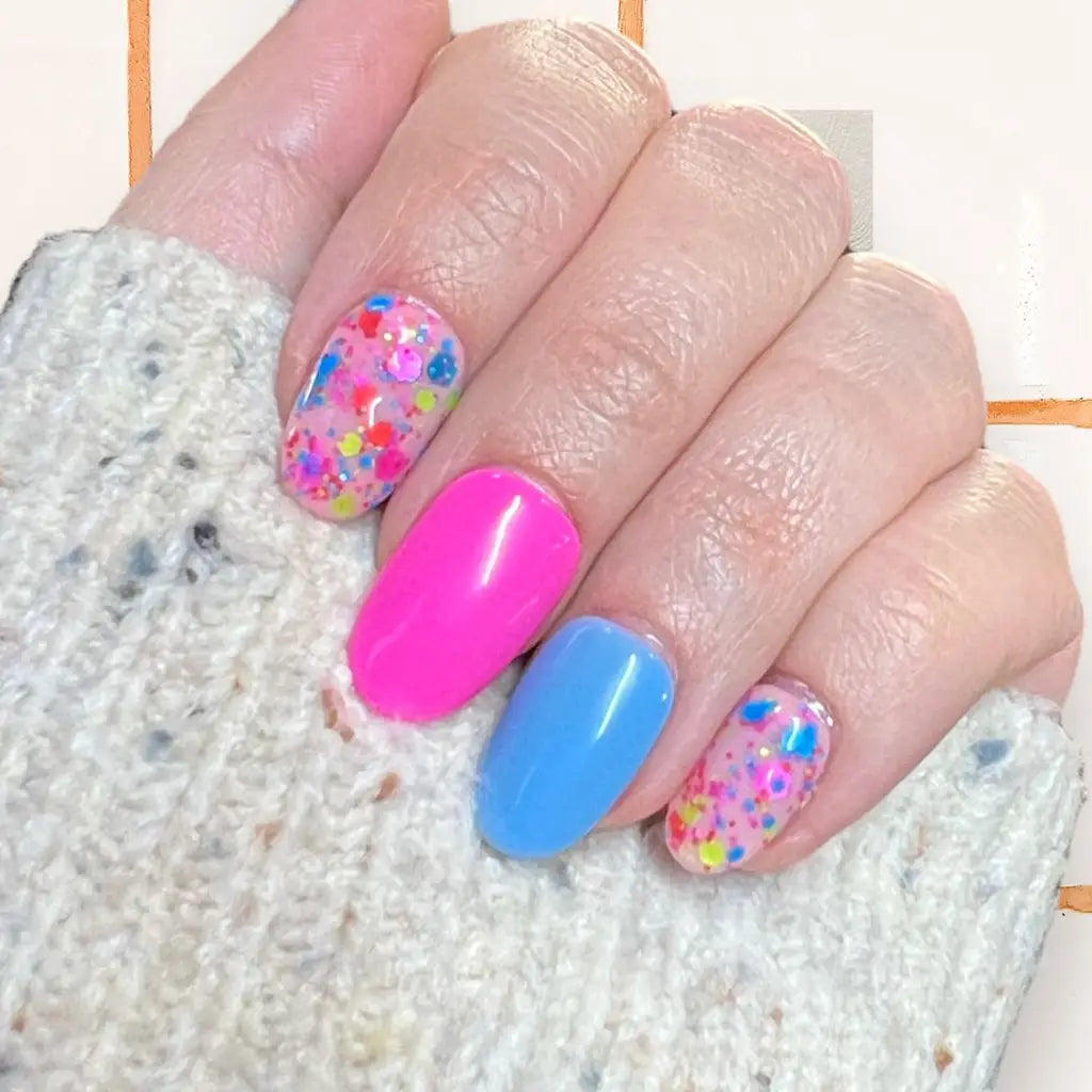 Colorful Party Popper-inspired nails with pink, blue, and multicolored confetti designs on a hand over a knitted background.