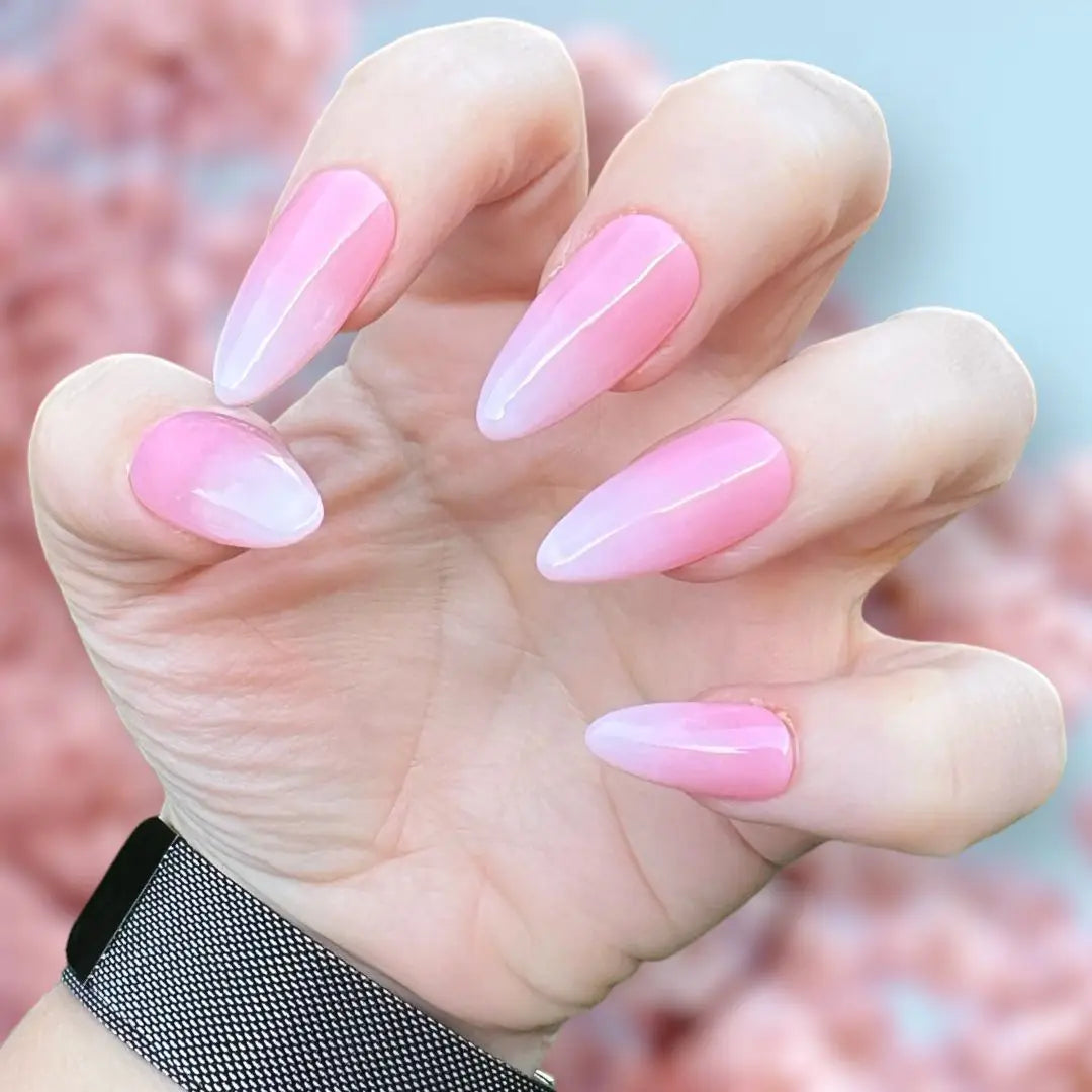 Hand displaying pink gradient baby boomer press-on nails with a soft pastel background.